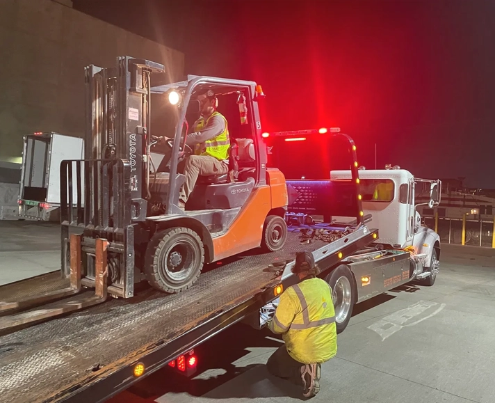 A tow truck is towing a large forklift.