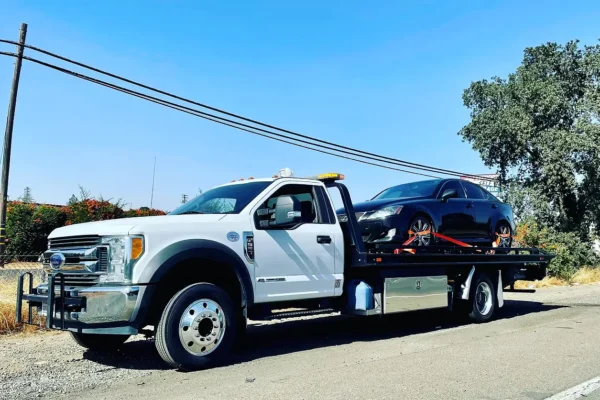 A white tow truck with a black car on the back