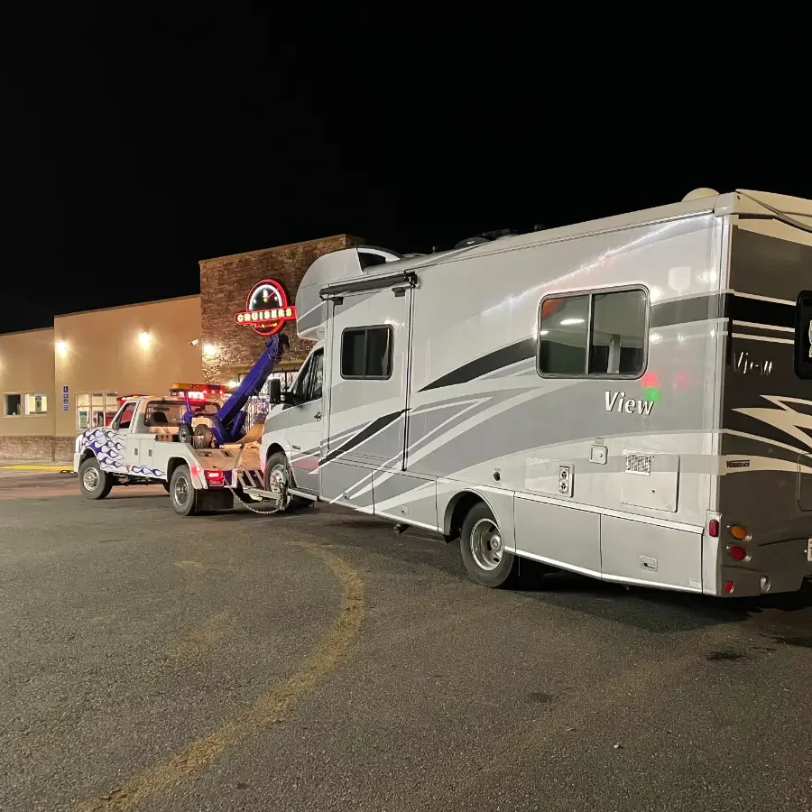 A tow truck towing an rv in the parking lot.