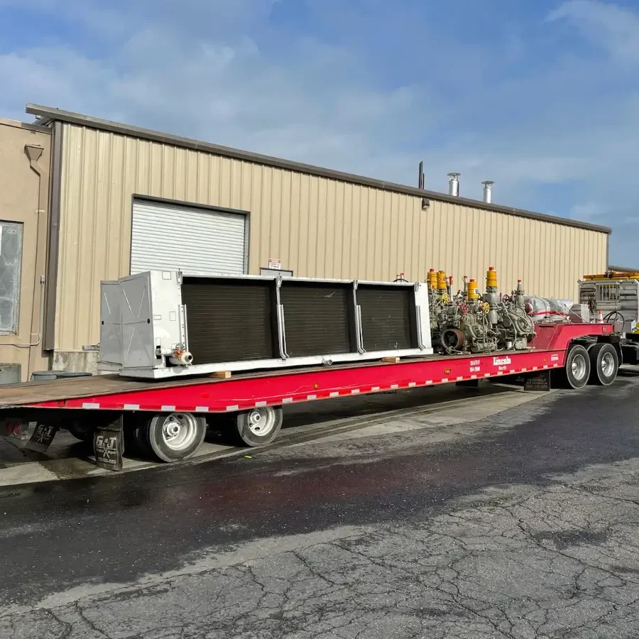 A red flatbed truck with a large trailer carrying an air conditioner.