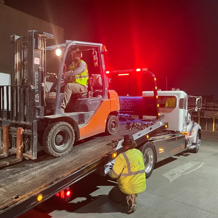 A tow truck is carrying a large forklift.